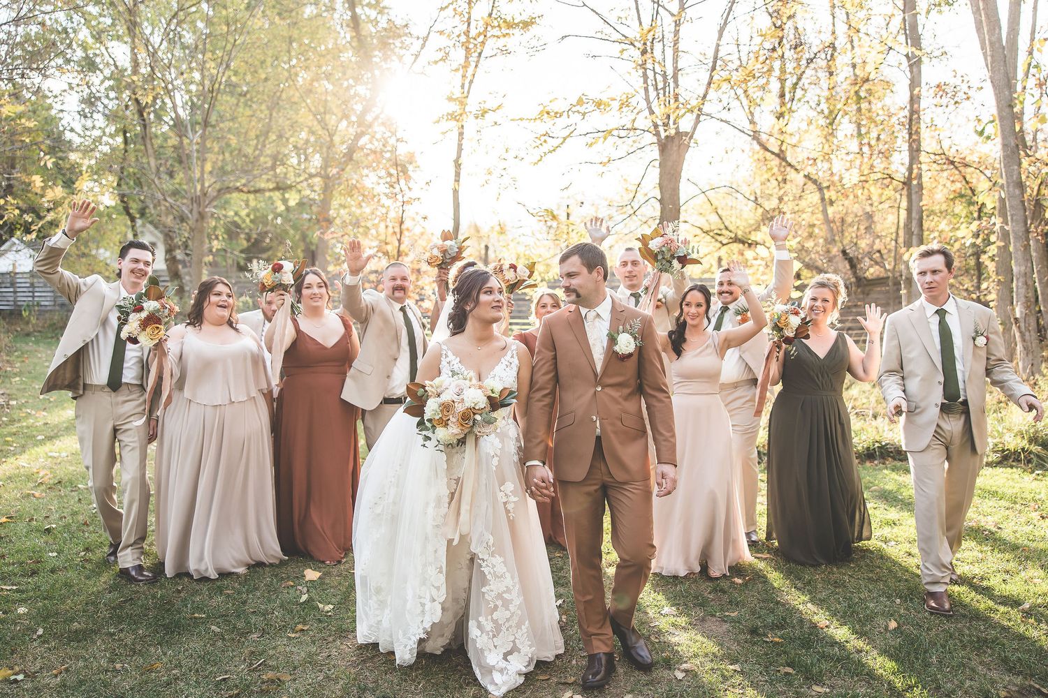 Wedding party poses in woodland setting with warm autumn sunlight filtering through trees.