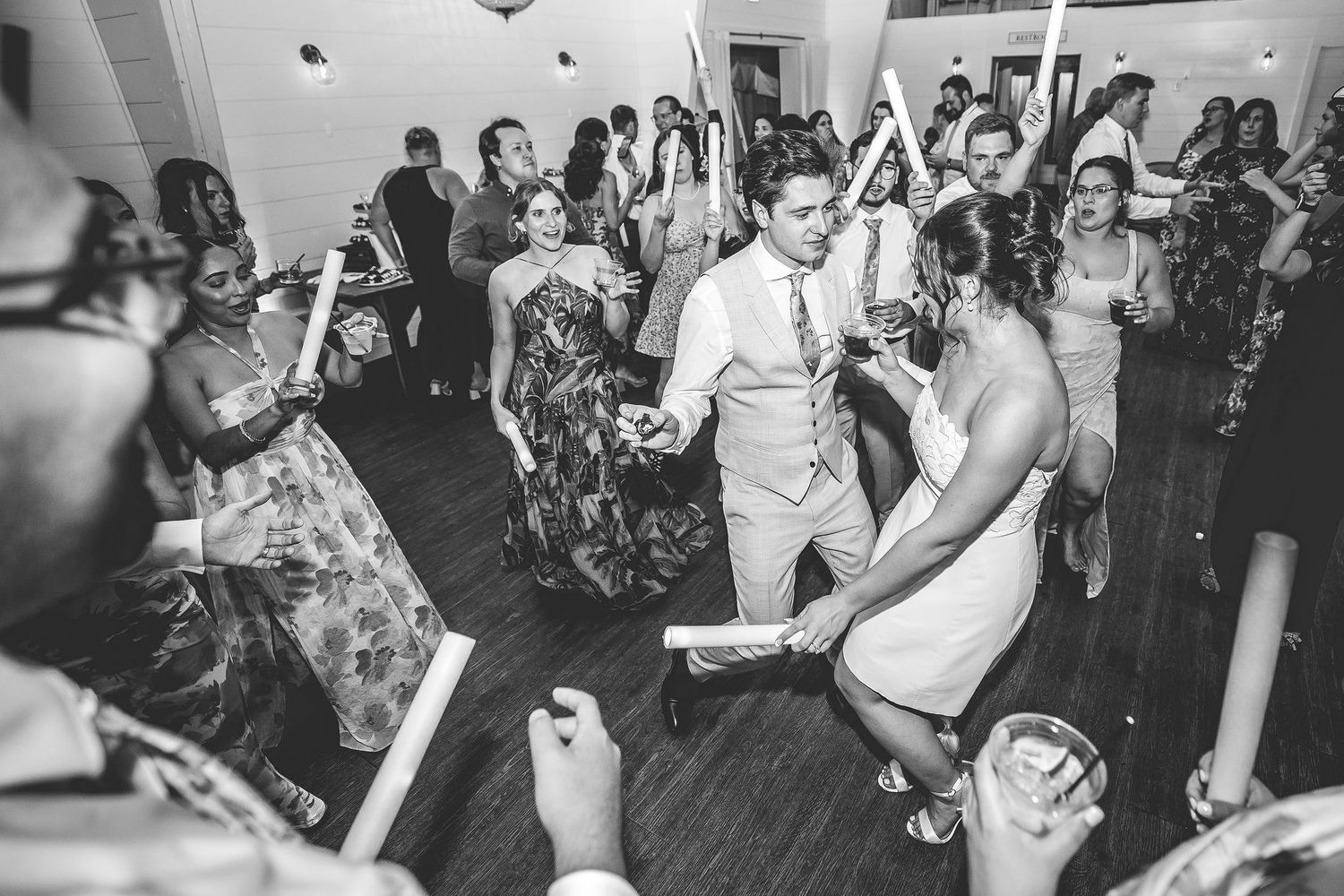Black and white photo of wedding guests dancing with light-up foam sticks.