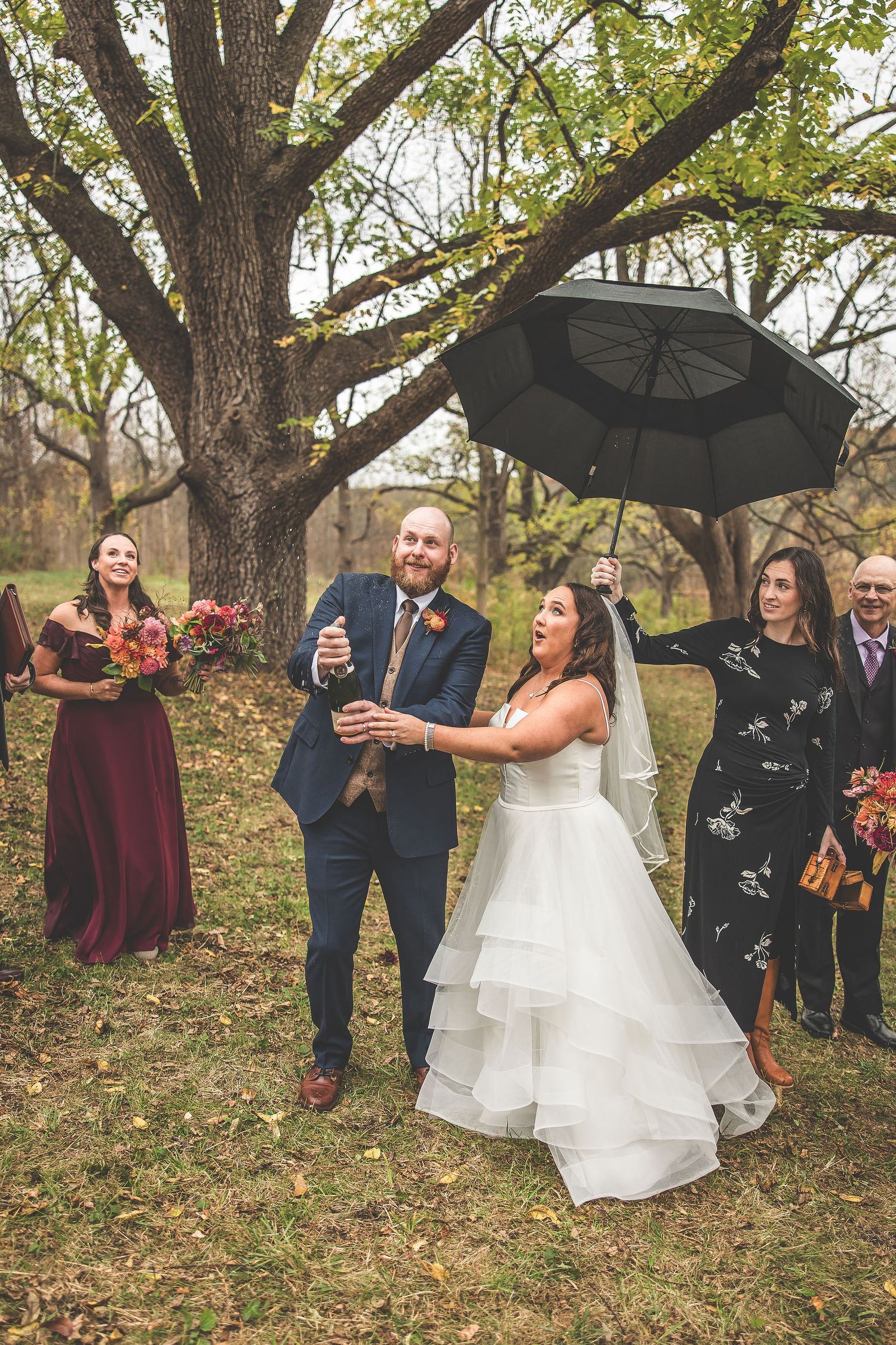 Wedding celebration candid moments captured under autumn trees with black umbrellas.