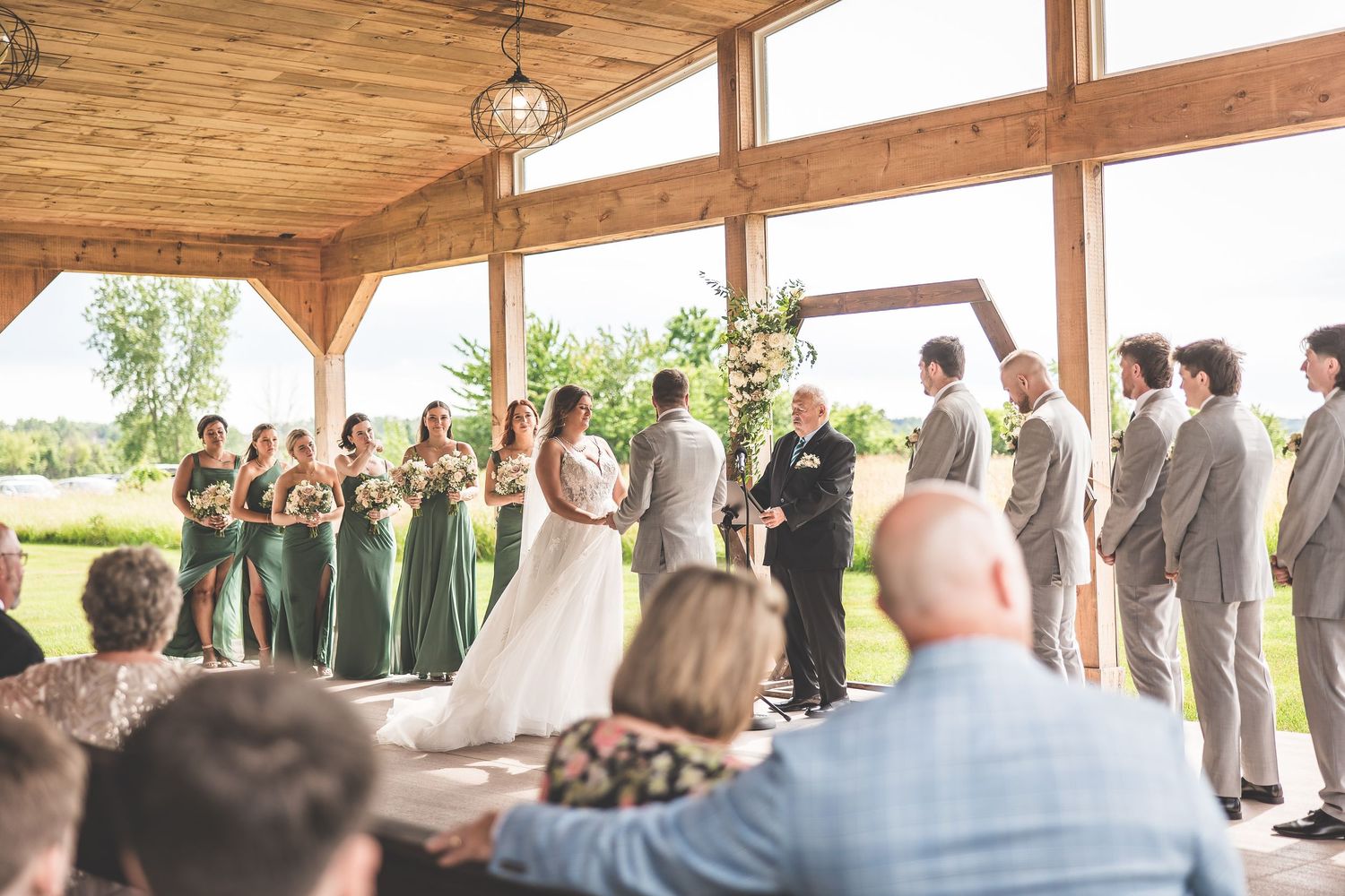 Wedding ceremony under wooden pavilion with guests seated and wedding party at the altar.