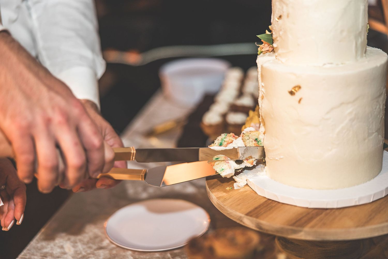 Close-up of wedding cake being cut and served on wooden plates.