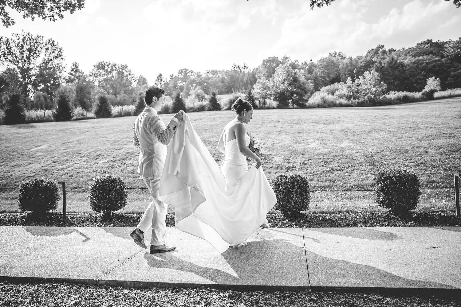 Flowing white wedding dress trails across a lush green hillside landscape.