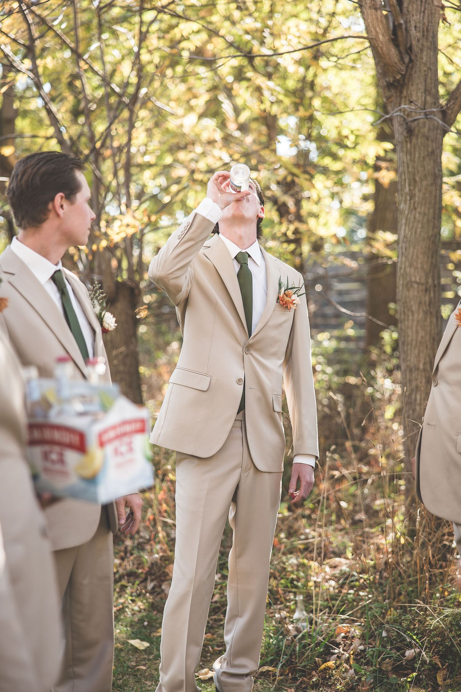 Groomsmen in tan suits sharing a celebratory moment in a wooded outdoor setting.