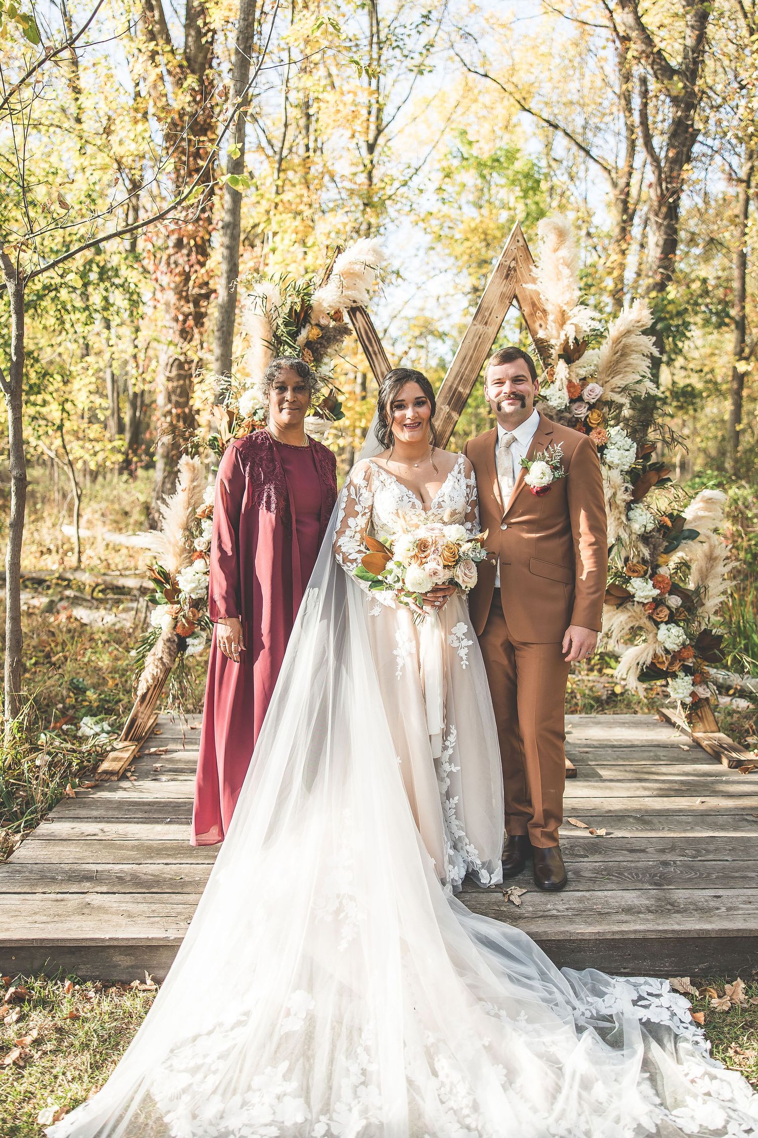 Wedding party posing outdoors with rustic wooden arch and autumn floral decorations.