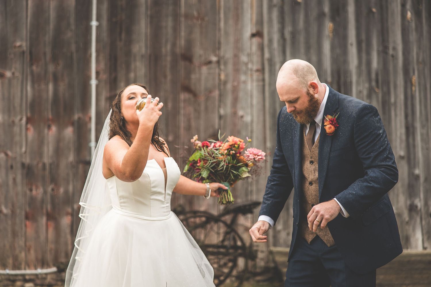 Wedding couple dances and laughs together in front of a rustic barn setting.
