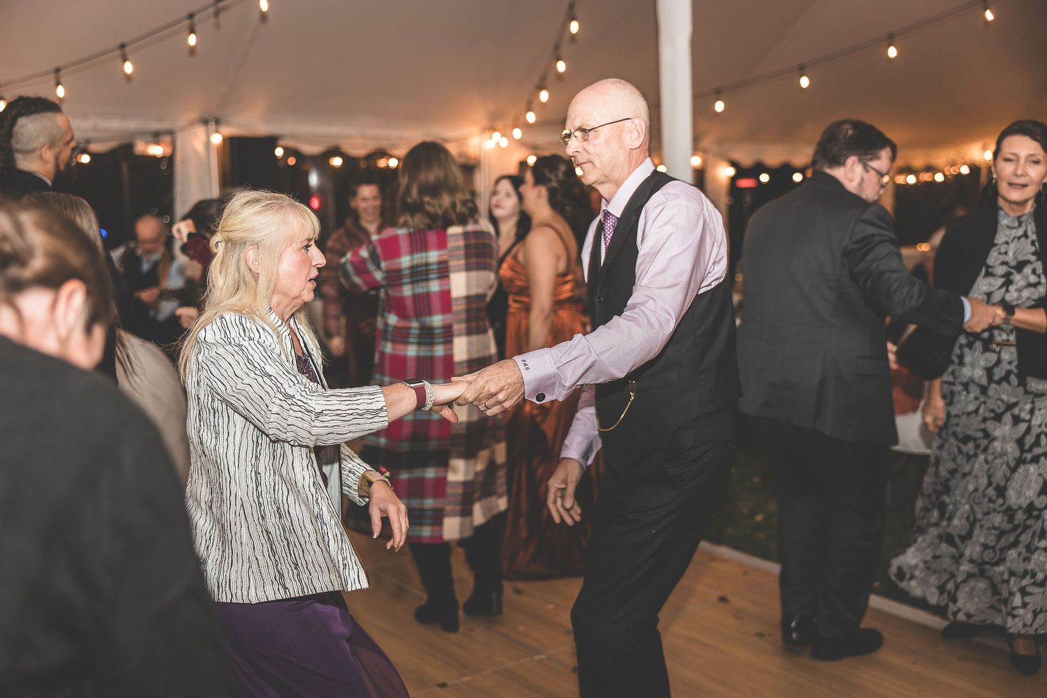 Couples dancing and celebrating at a wedding reception with string lights creating a romantic atmosphere.