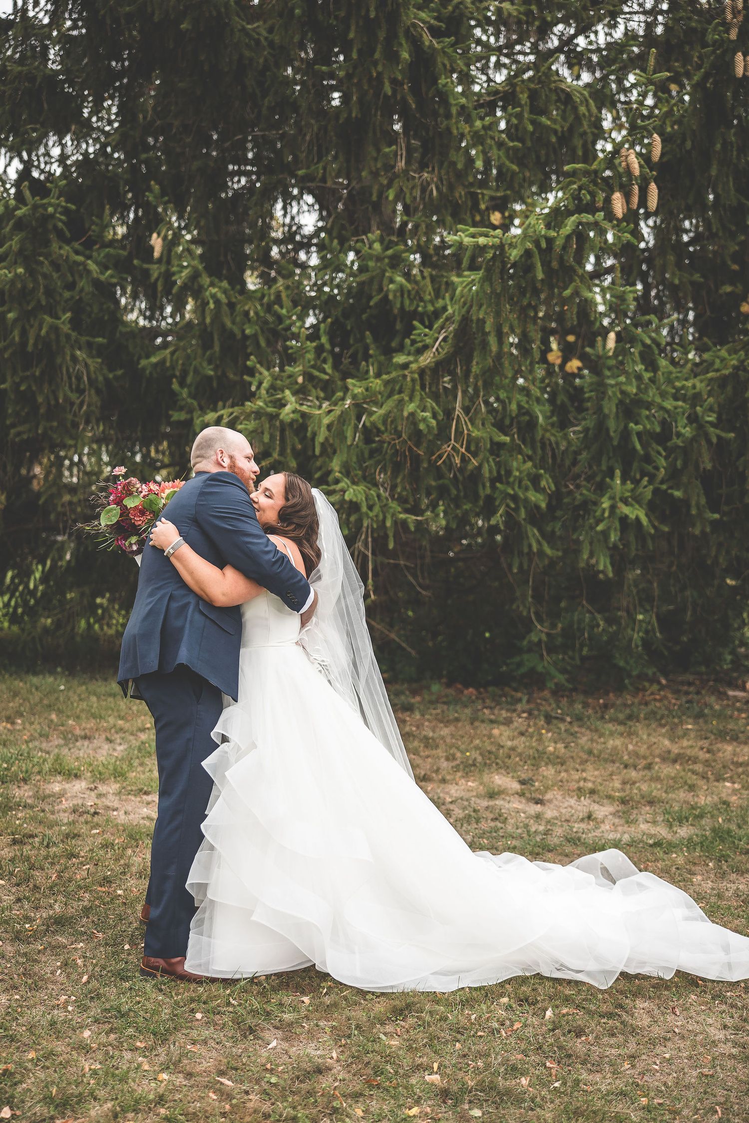 An intimate first look moment between newlyweds with a flowing white dress against evergreen trees.