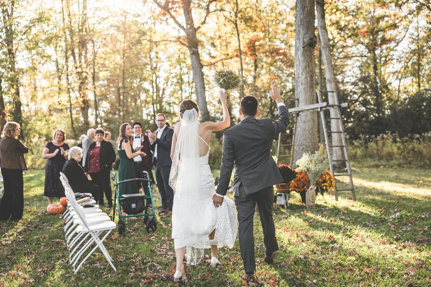 Outdoor autumn wedding ceremony with guests seated among trees and natural fall decorations.
