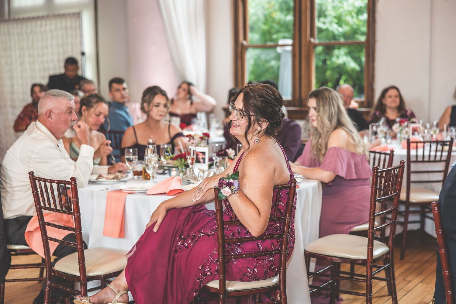 Reception guests enjoy dinner and conversation at tables decorated in burgundy and white.
