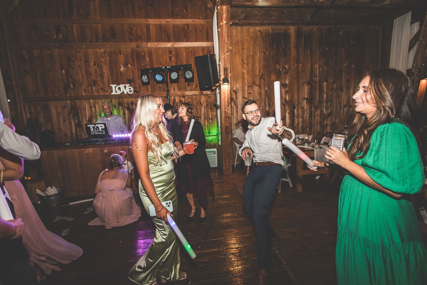 Guests in formal attire dancing at a rustic barn wedding reception with atmospheric lighting.