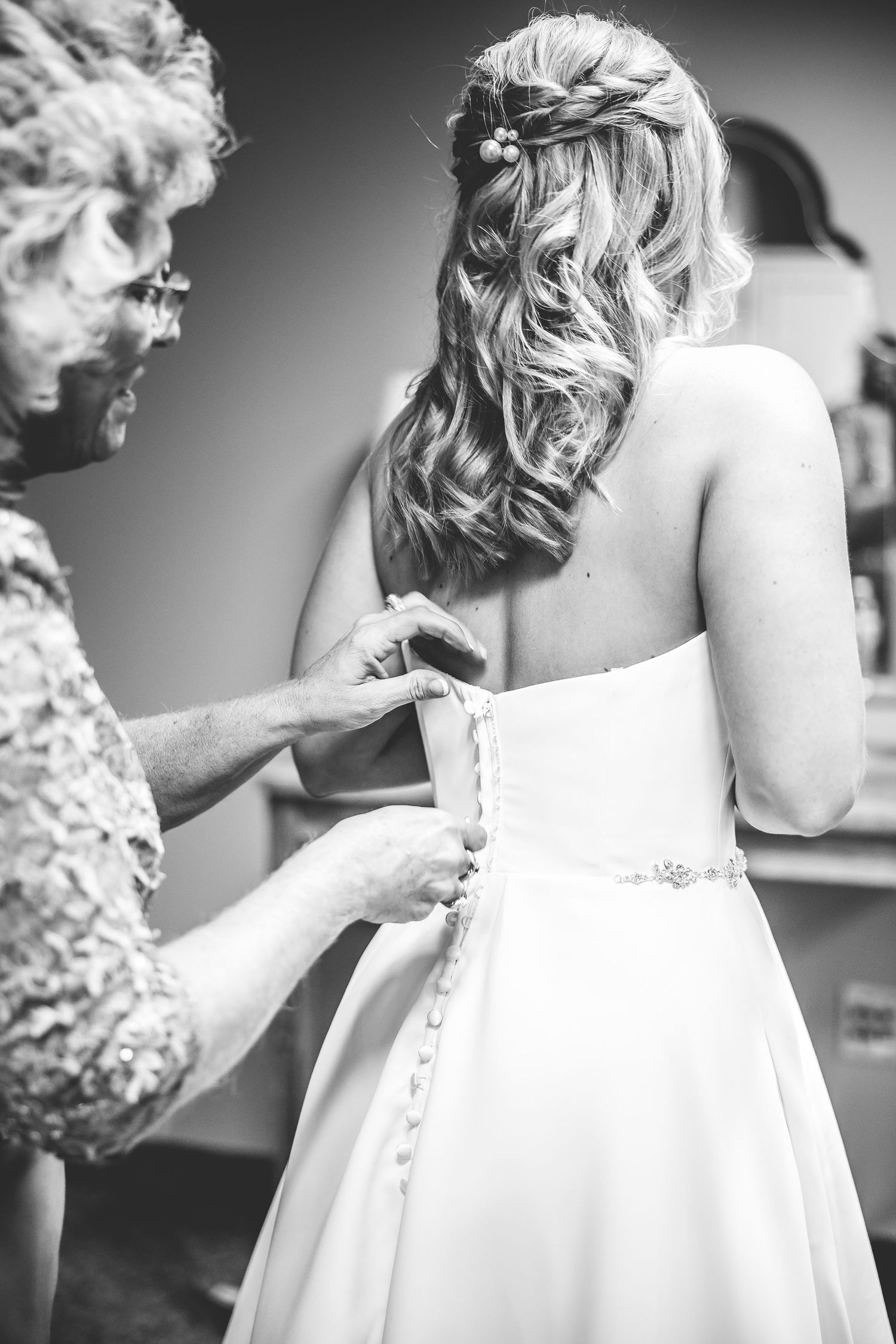 Black and white photo showing the intricate details of buttoning up a wedding dress.