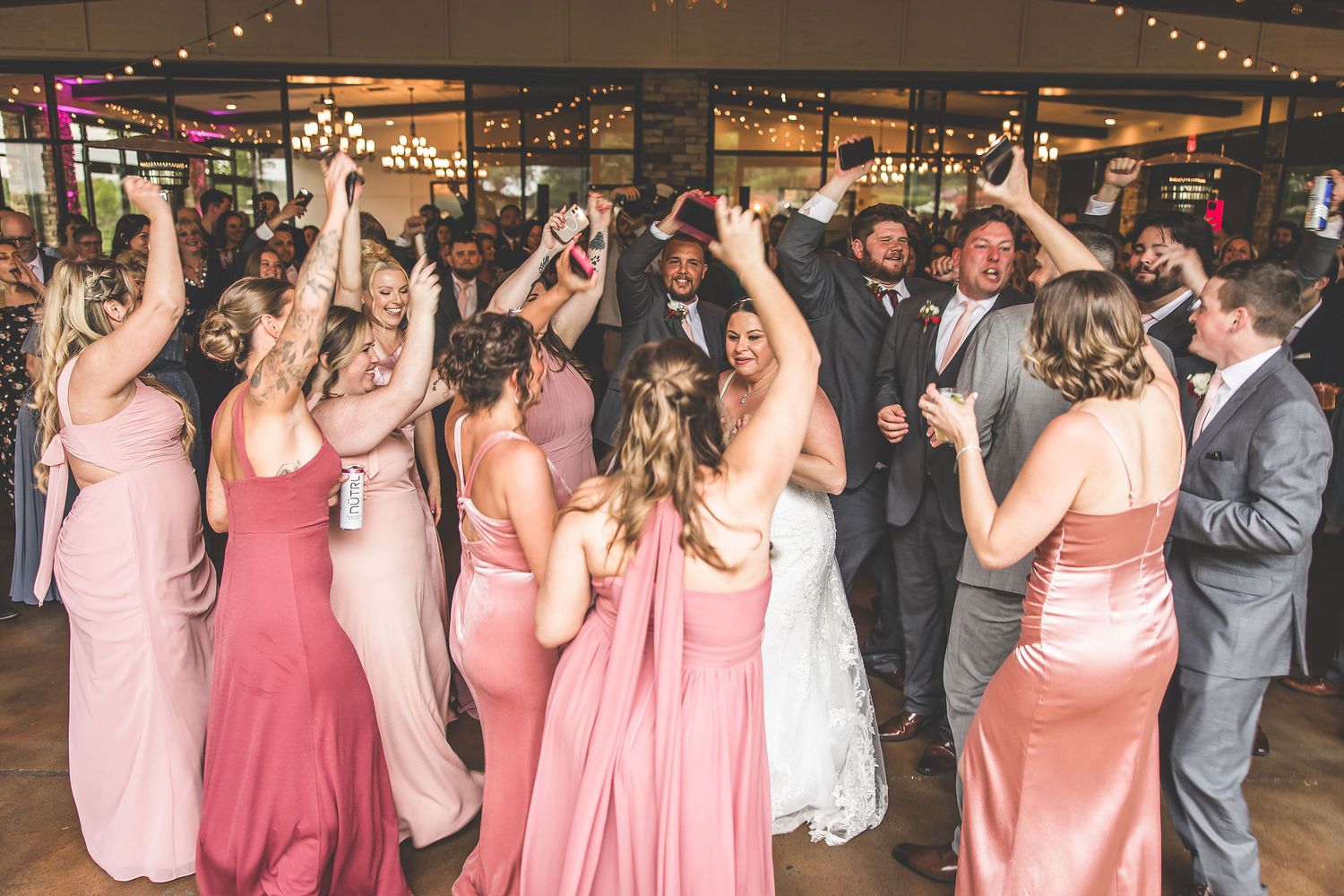 Wedding guests in pink dresses and grey suits dance together at a reception.