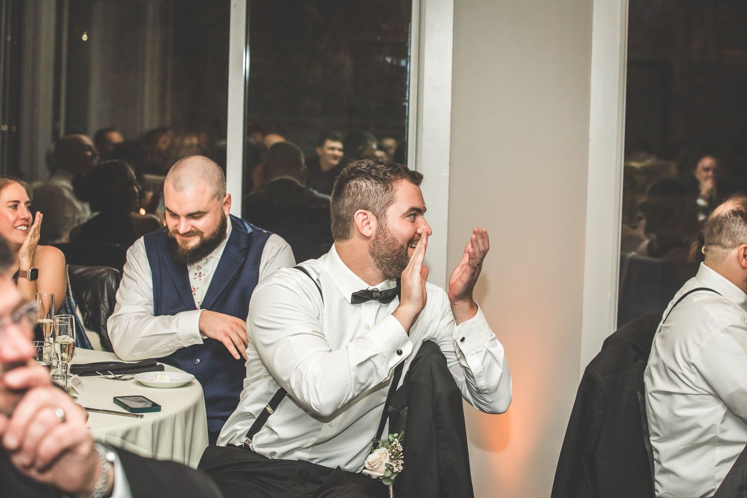 Wedding guests in white dress shirts laugh and socialize at reception tables.