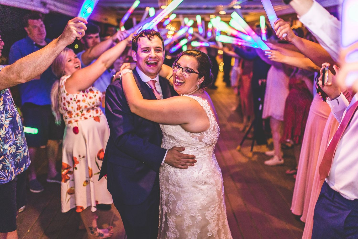 Festive dance floor scene with colorful lighting and celebratory atmosphere at a wedding reception.