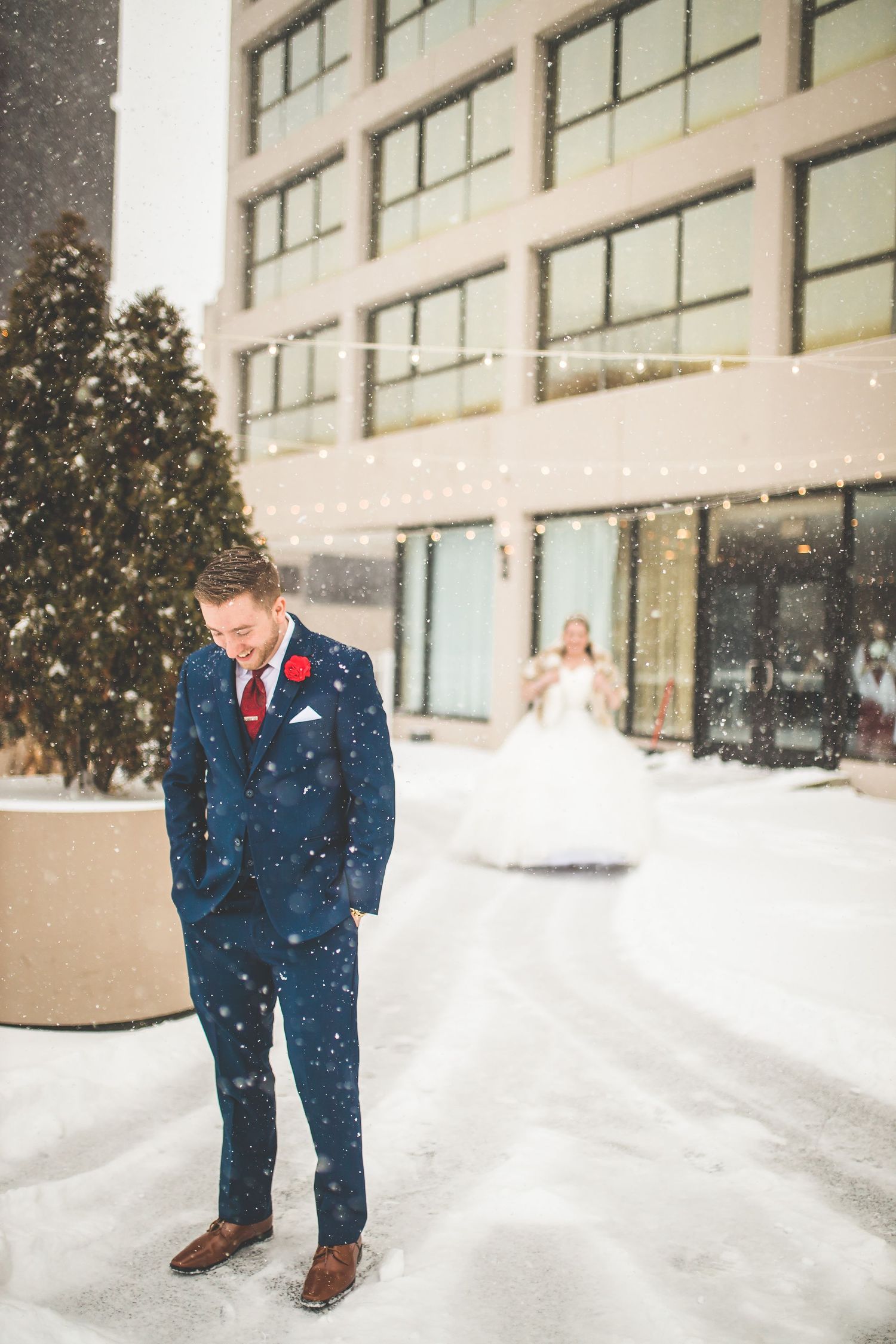 Winter wedding scene with snow falling outside a modern building.