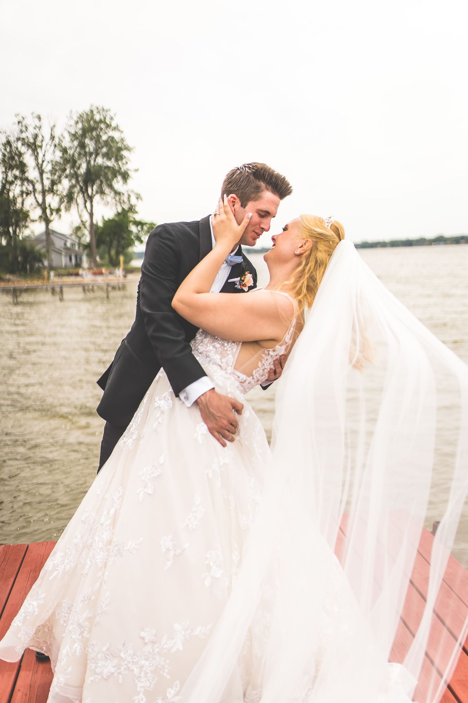 Romantic wedding couple embraces on wooden dock by the water.