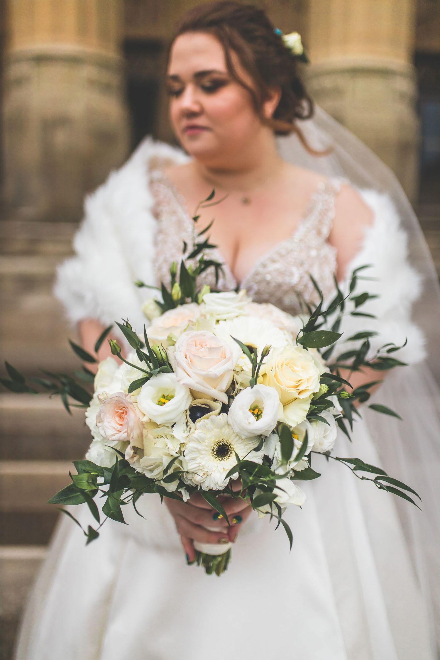 Close-up of white and blush wedding bouquet with roses and greenery.