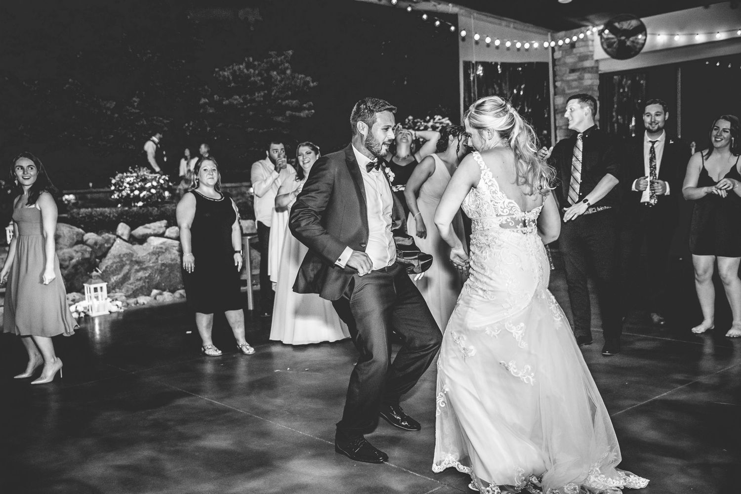 Black and white photo of couple dancing at their wedding reception under ambient lighting.
