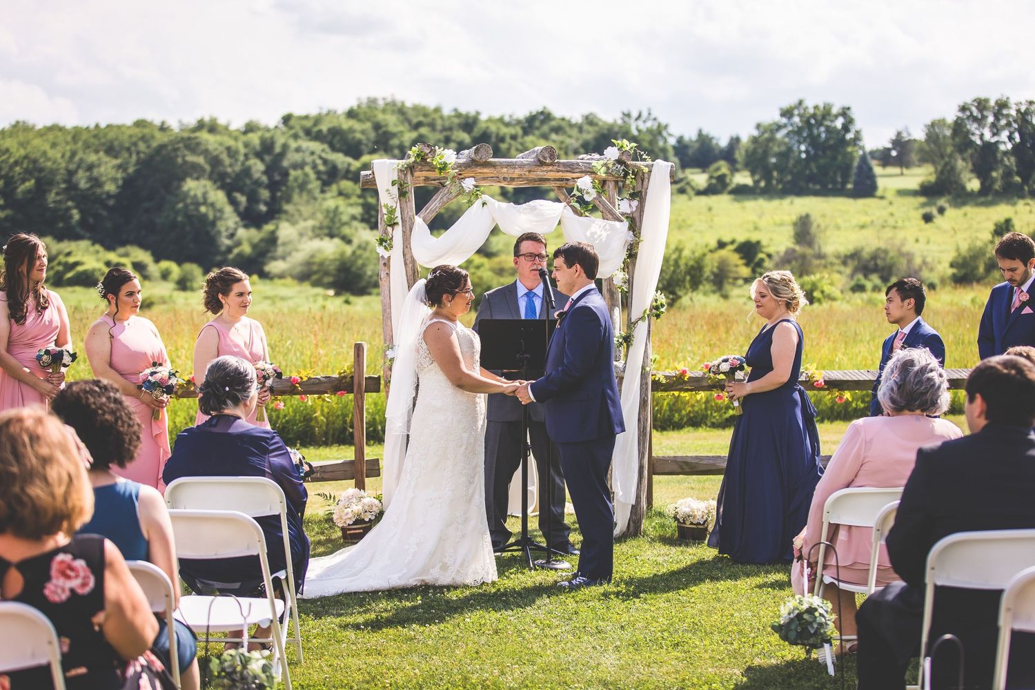 Panoramic view of an outdoor wedding ceremony with guests seated in white chairs.