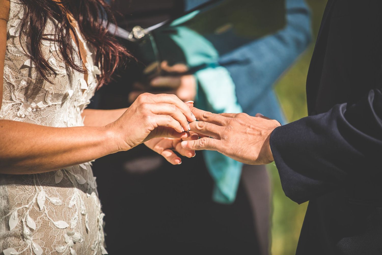 Close-up shots of hands exchanging rings during an outdoor ceremony.