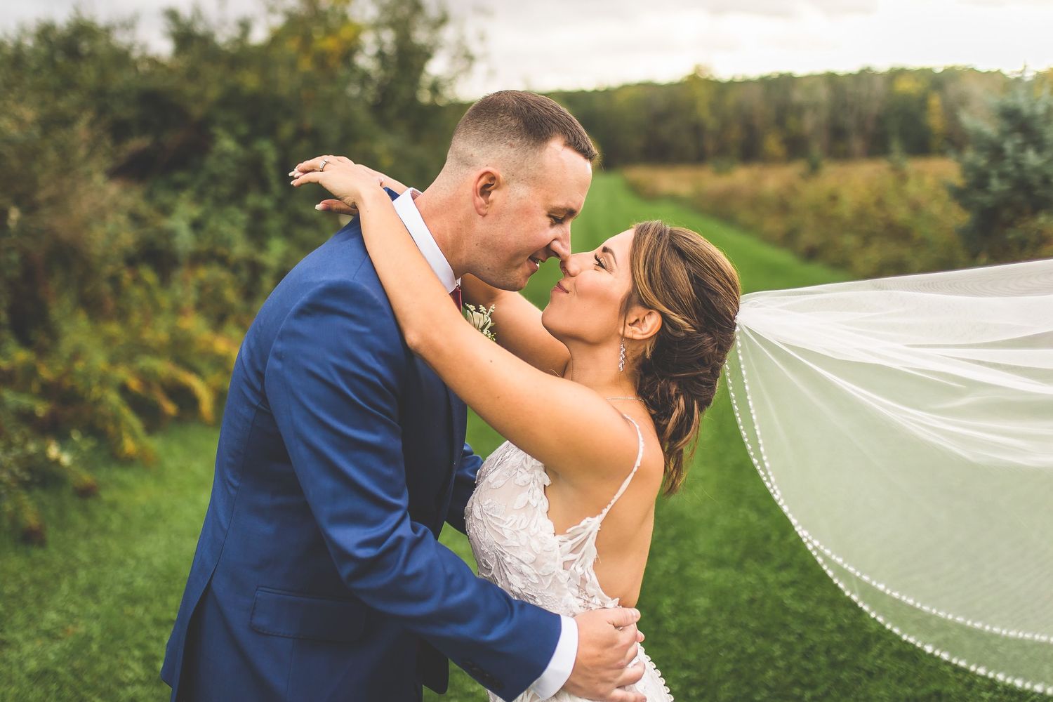 Wedding couple shares intimate moments with flowing veil in outdoor setting.