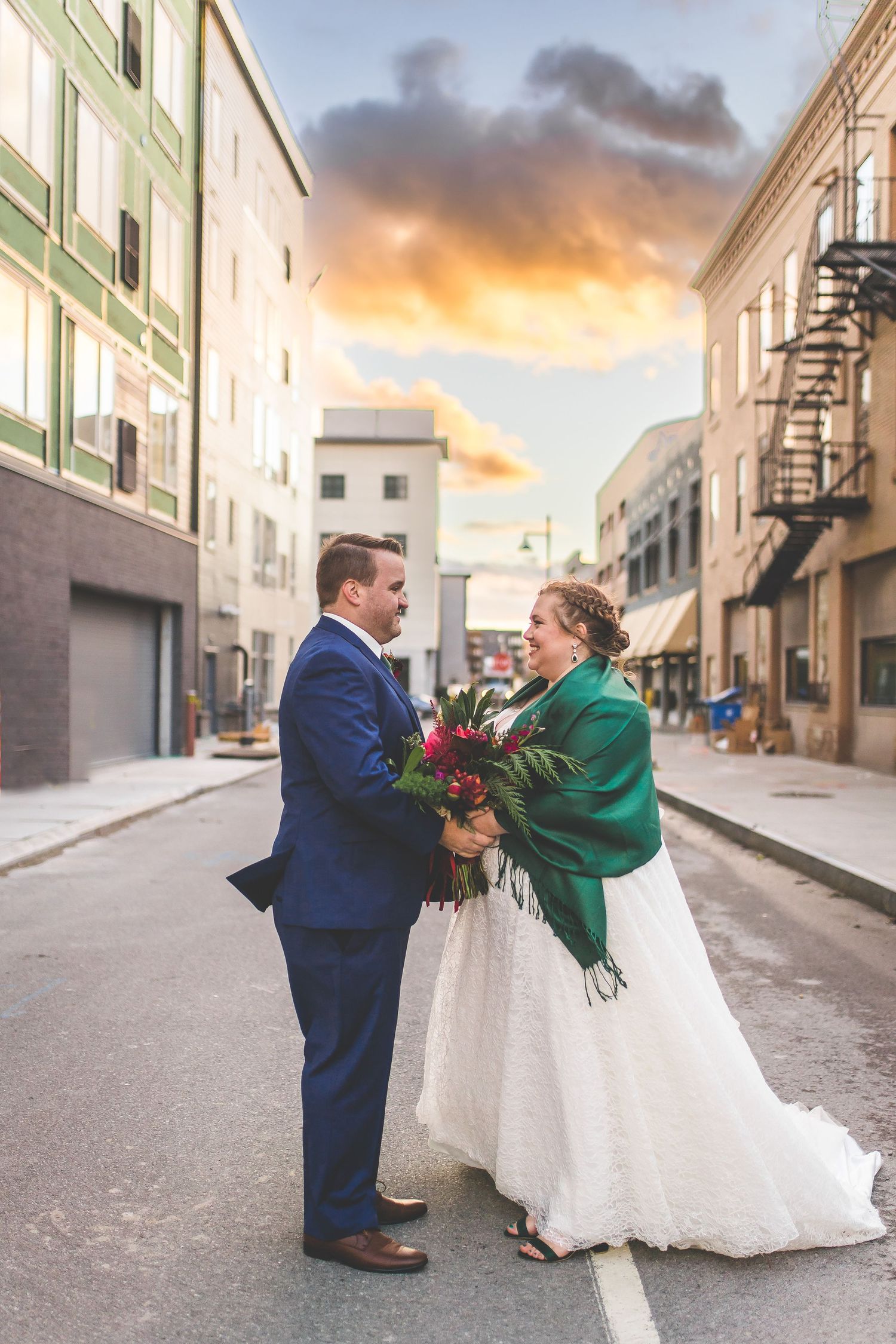 A couple shares a romantic moment on an urban street at sunset, with the bride wearing a white gown and emerald shawl.