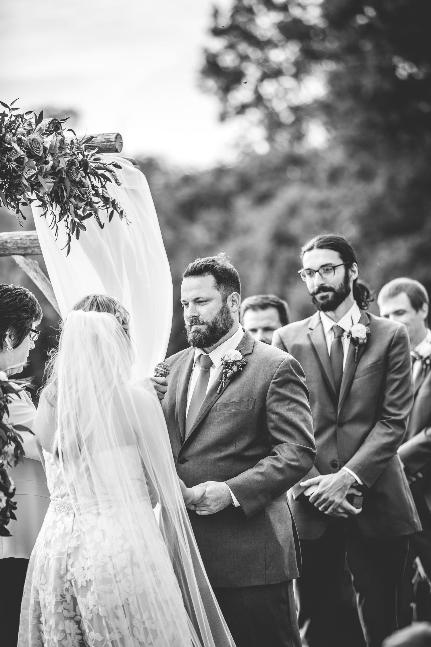 Black and white capture of emotional wedding ceremony moments under floral-decorated arch.