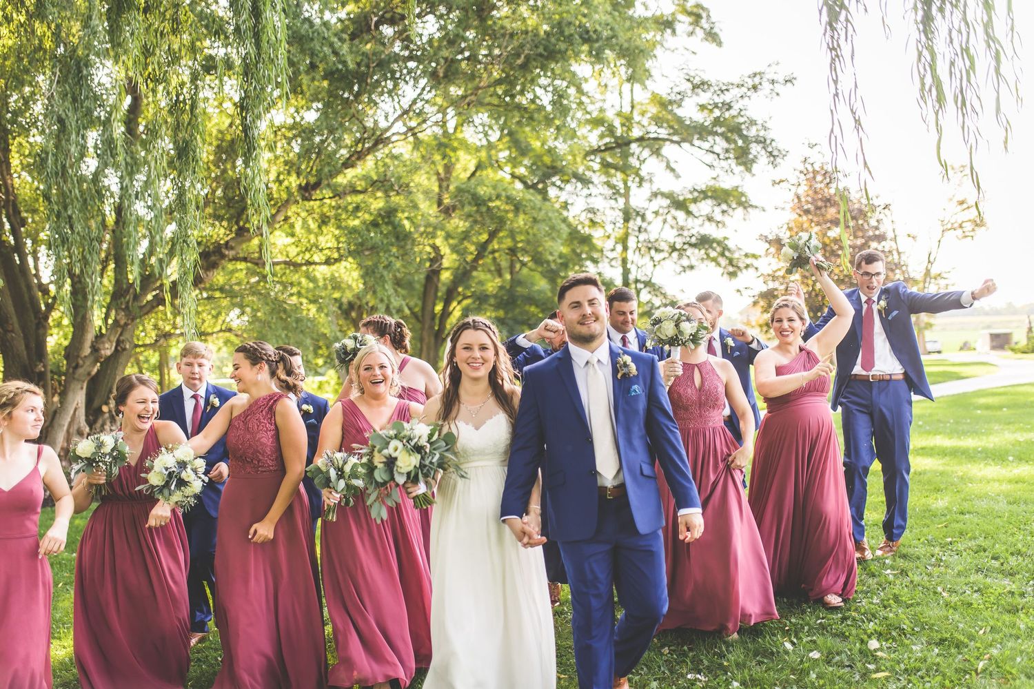 Wedding party in burgundy dresses and navy suits pose together in outdoor garden setting.