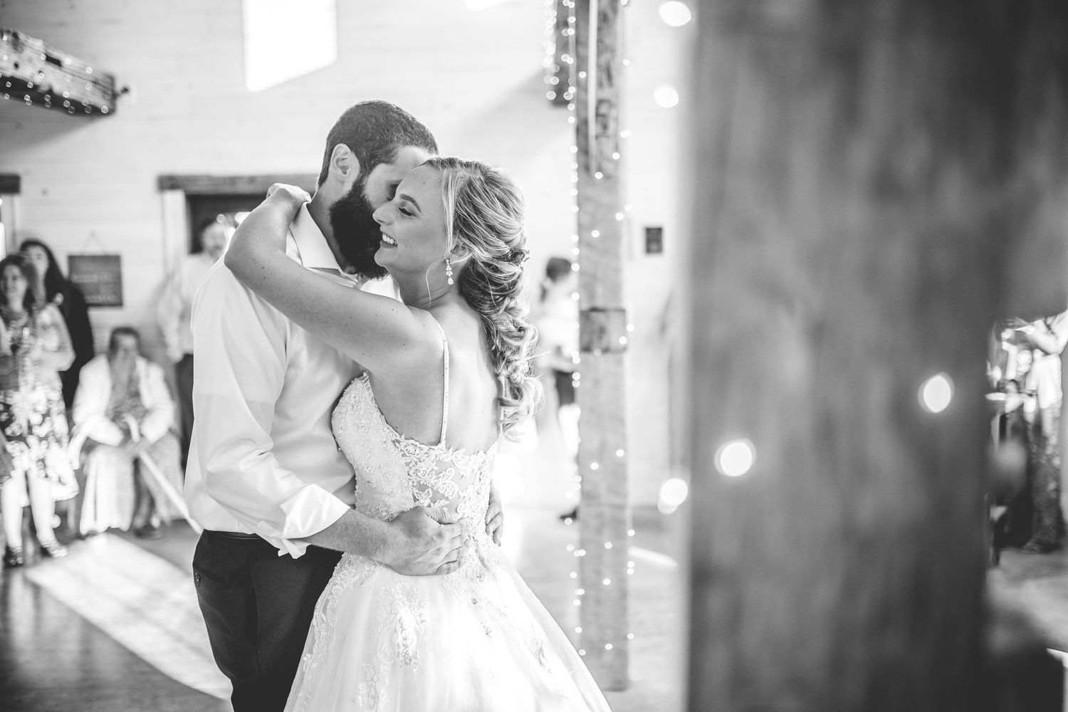 Black and white photo of newlyweds dancing intimately in a rustic venue with wooden beams.
