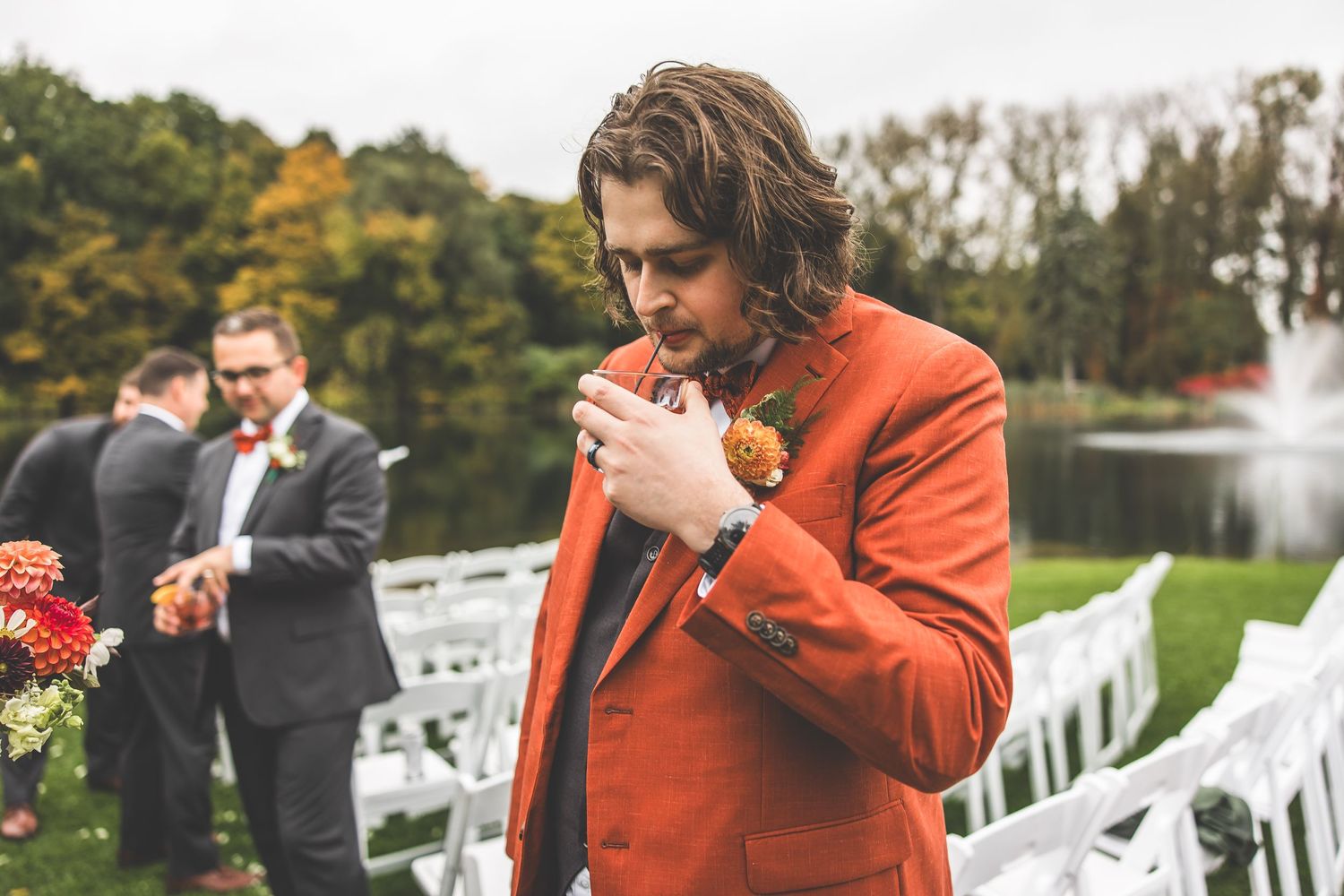 A wedding ceremony takes place outdoors with white chairs and fall foliage creating a scenic backdrop.