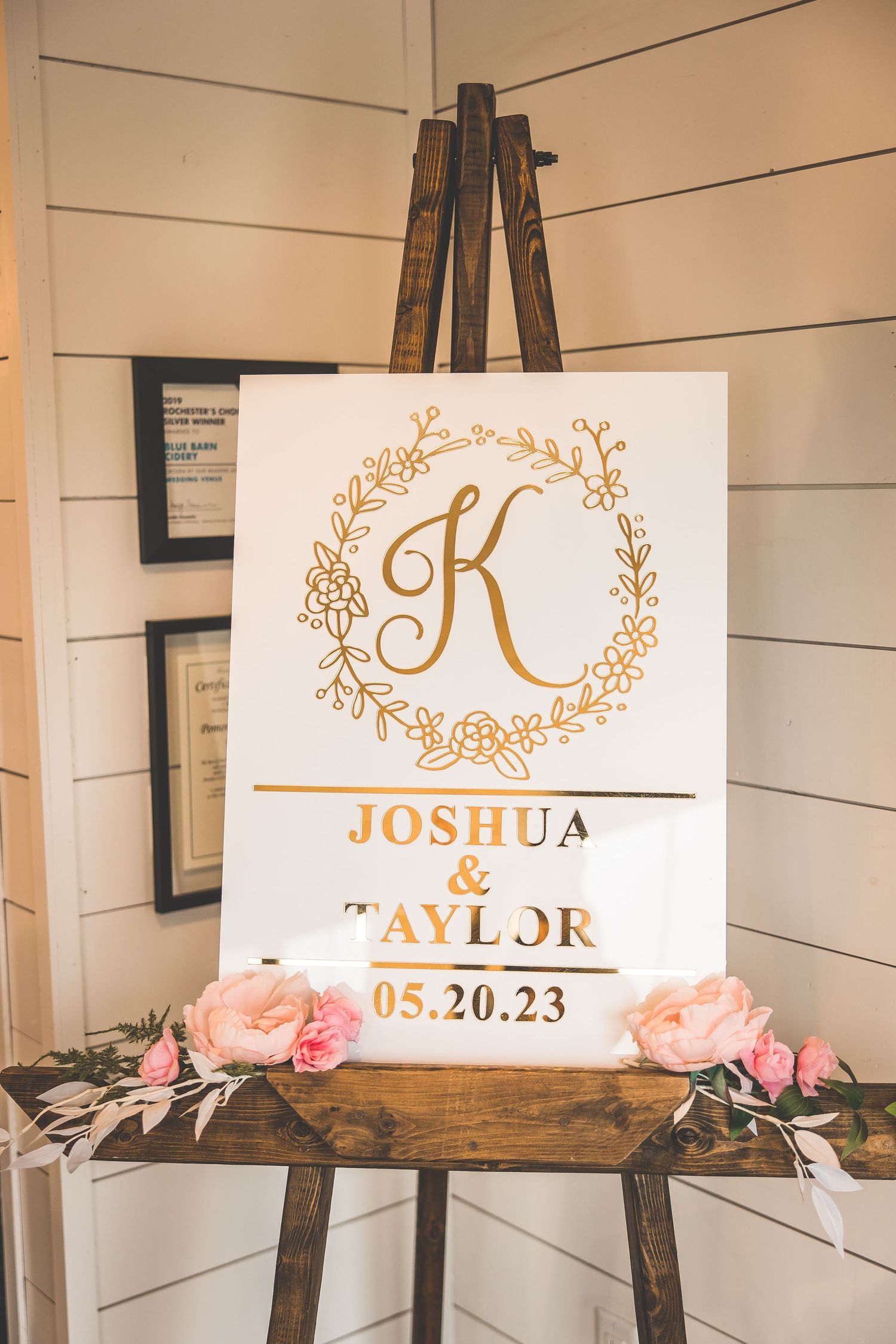 A wedding welcome sign with gold monogram and couple's names displayed on a wooden easel.