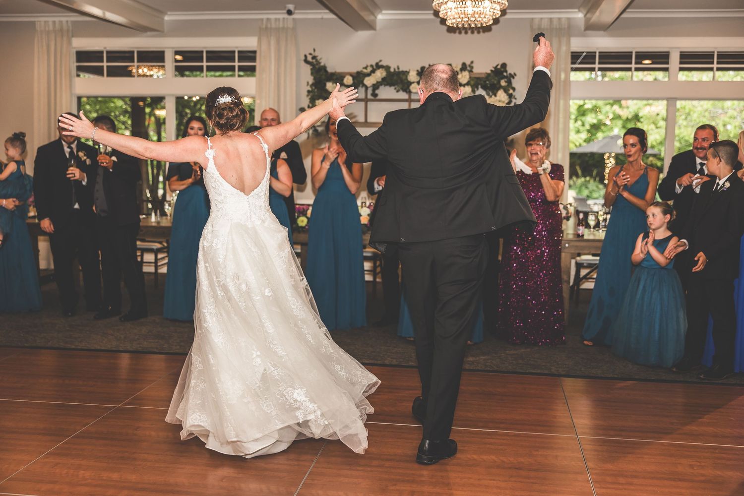Wedding reception dance floor filled with celebrating guests under elegant chandeliers.