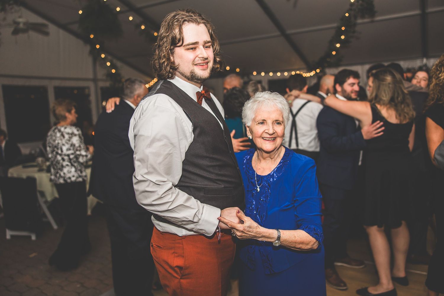Wedding guests dancing and laughing together during evening reception celebrations.