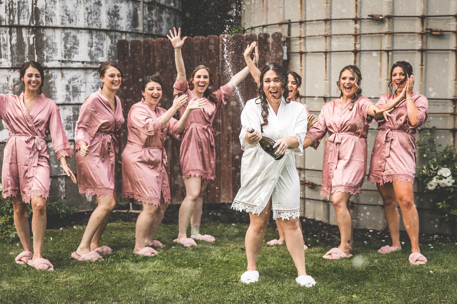 Wedding party in pink robes and white dress pose playfully outdoors.