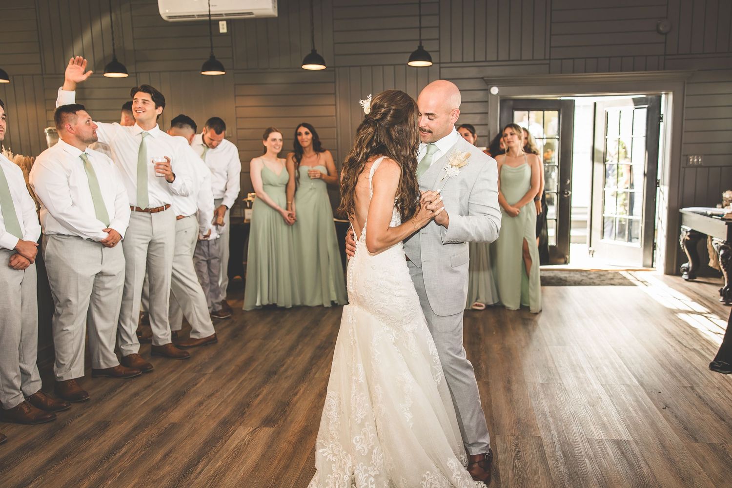 Wedding reception venue with dark walls and hardwood floors filled with dancing guests.