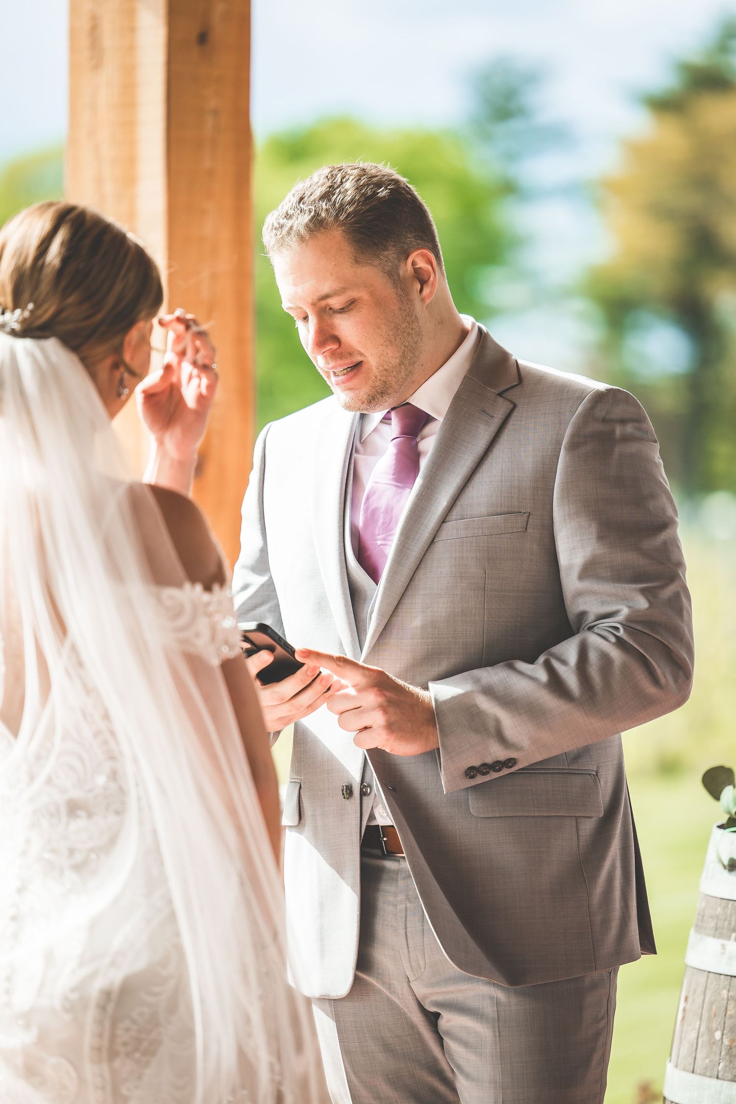 Wedding couple exchanging vows under wooden pavilion during outdoor ceremony.
