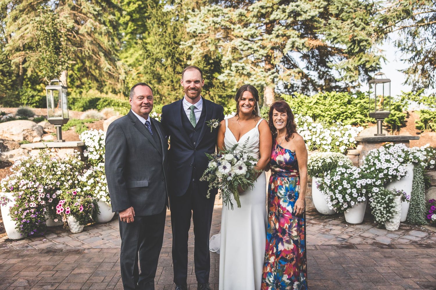 Wedding group portraits taken in a lush garden setting with white floral arrangements.