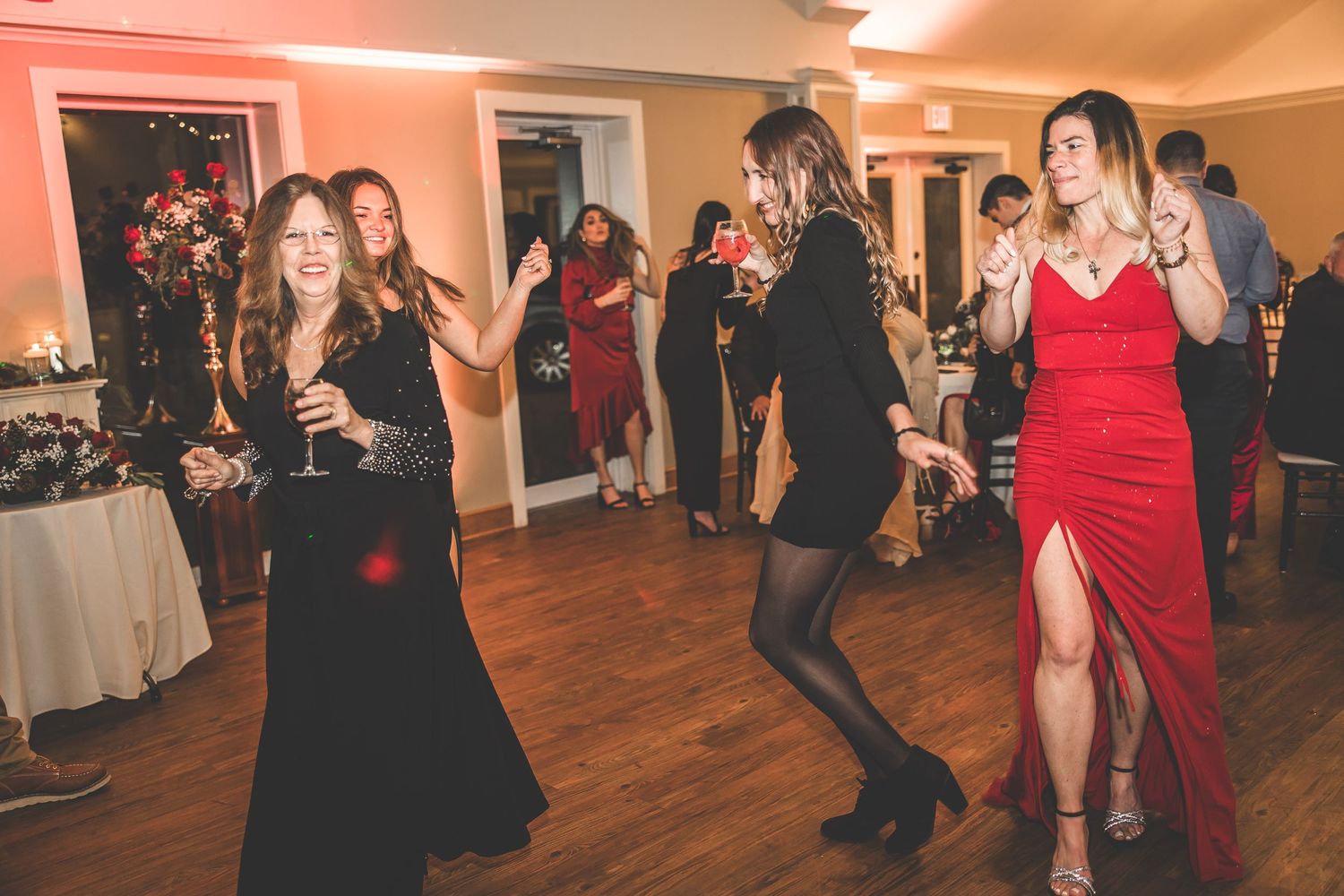 Guests dance and celebrate at an indoor wedding reception with warm lighting and hardwood floors.