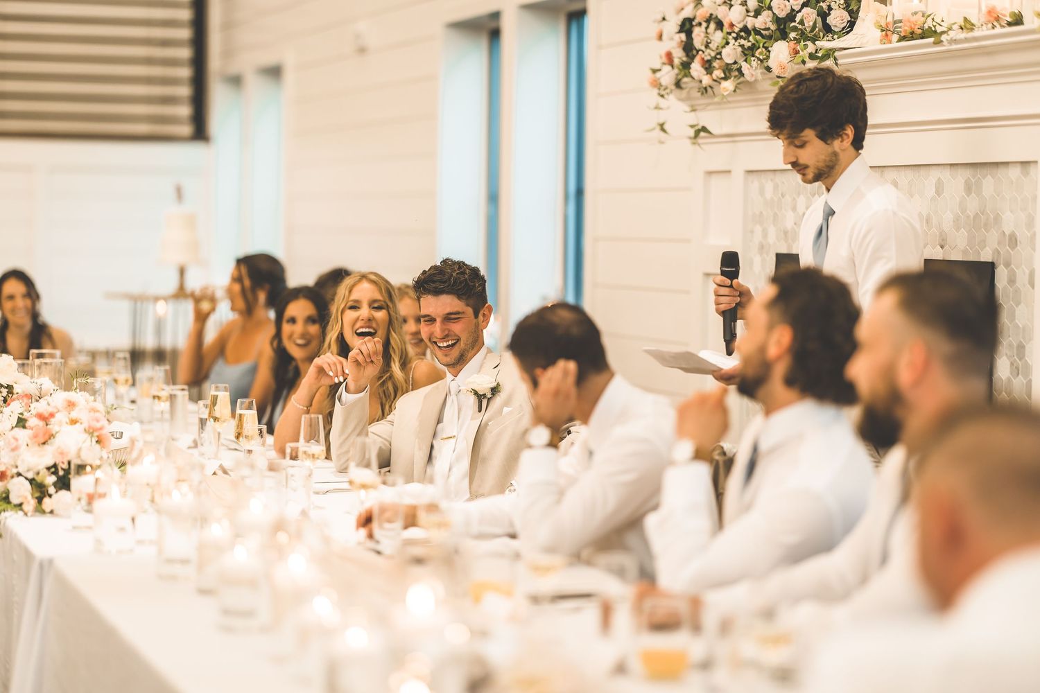 Wedding party and guests enjoying dinner at long tables decorated in white and floral arrangements.