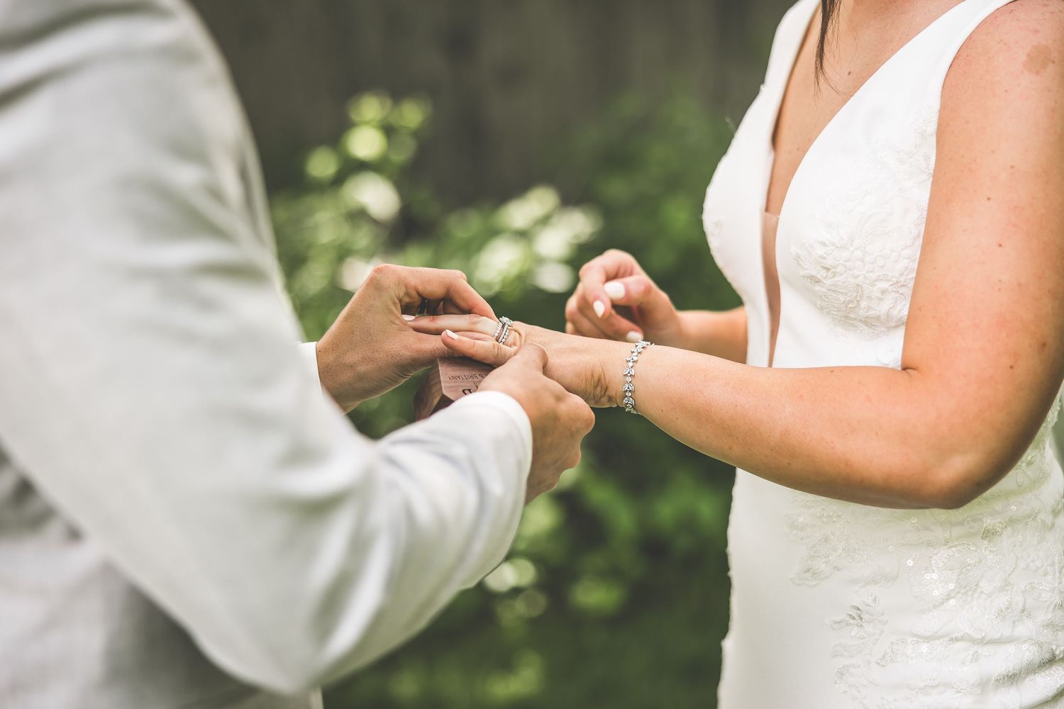 Elegant couple in white wedding attire pose together outdoors.
