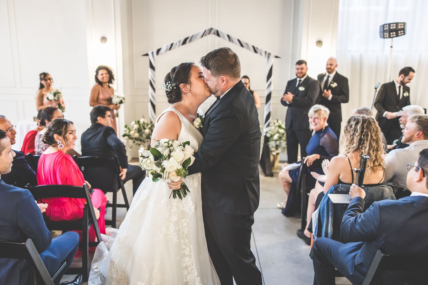 Wedding ceremony guests seated in rows watching the celebration in an elegant white venue.