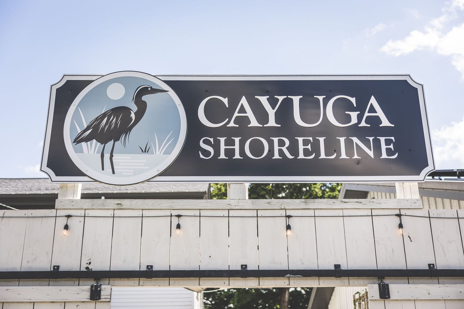 Cayuga Shoreline business signage mounted on white exterior wall with blue sky background.