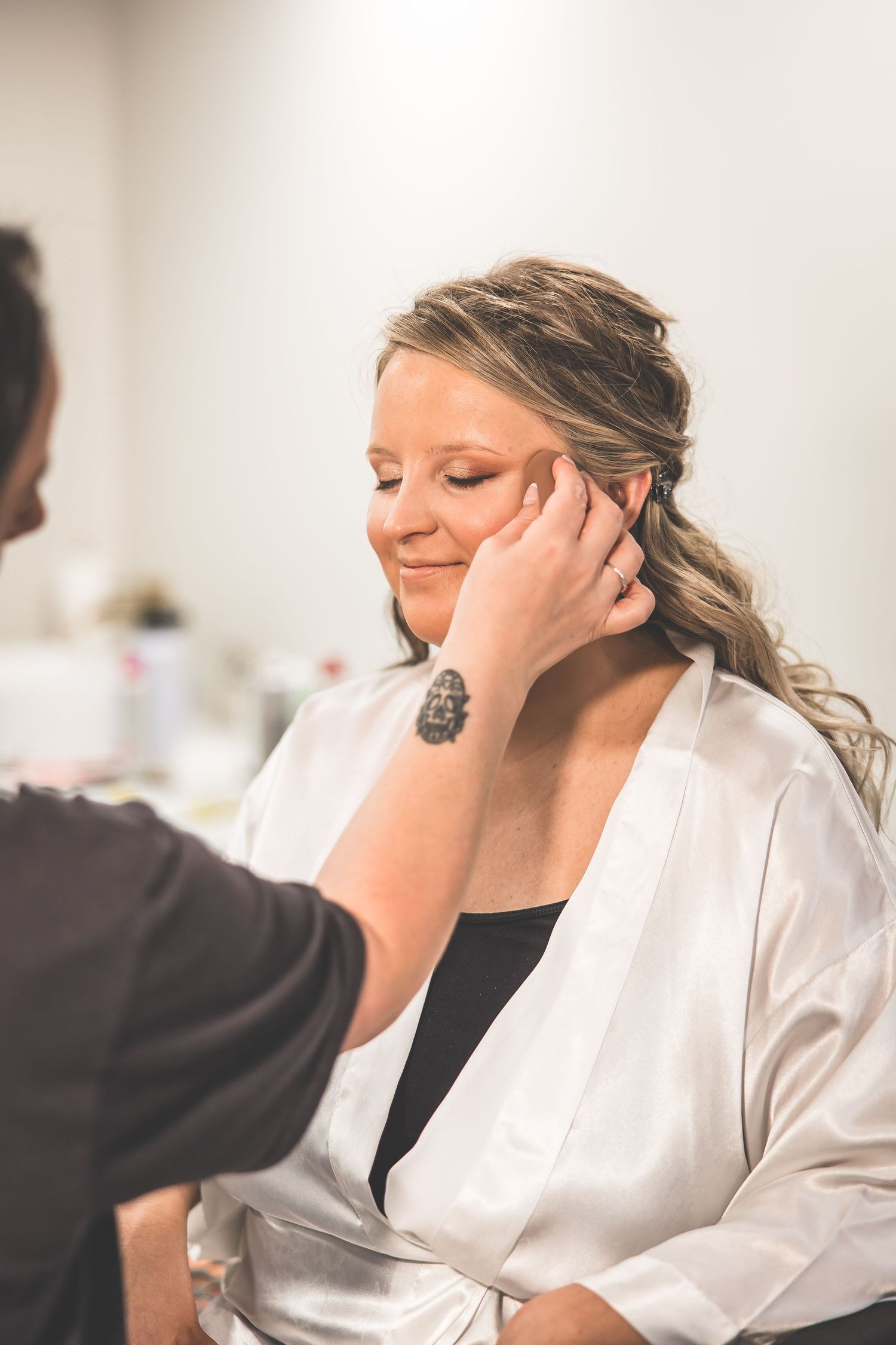 Wedding day preparation moment showing makeup application in a bright room.