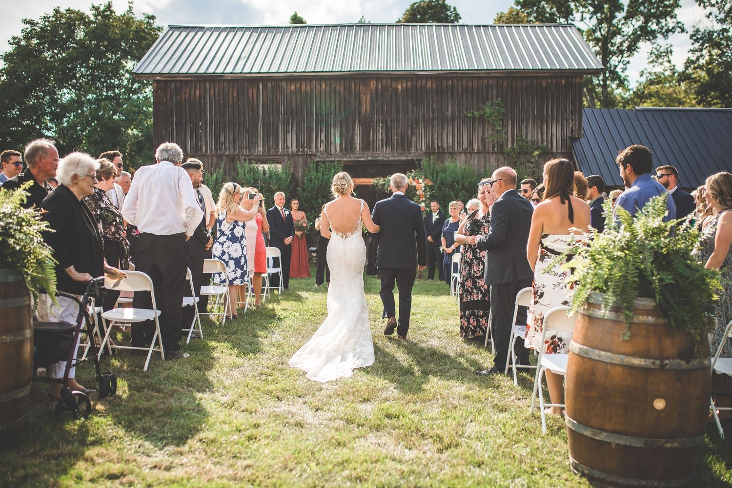Wedding recessional at rustic barn venue with guests lining the aisle.