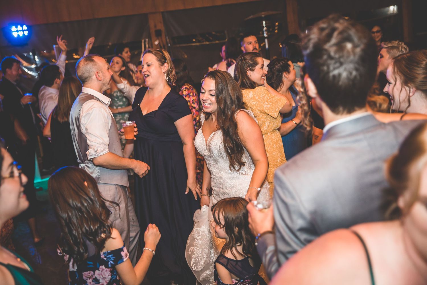 Wedding reception dance floor filled with celebrating guests under blue lighting.
