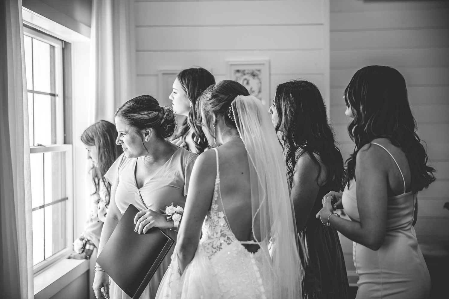 Black and white photo of wedding party members looking out a window together.