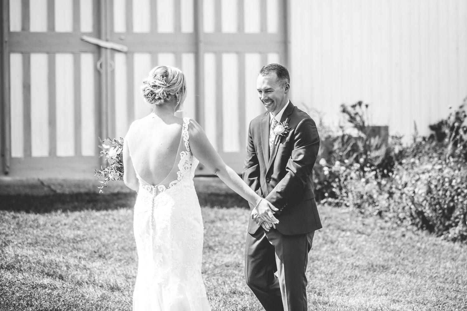 A black and white photo shows a couple sharing a playful moment in a garden setting.