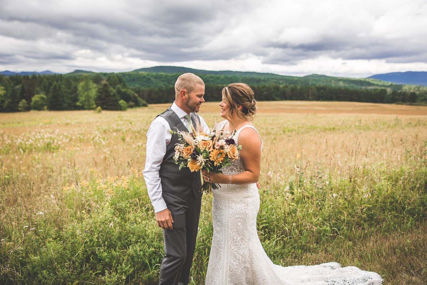 Romantic wedding portraits in a golden field with mountain backdrop and cloudy skies.