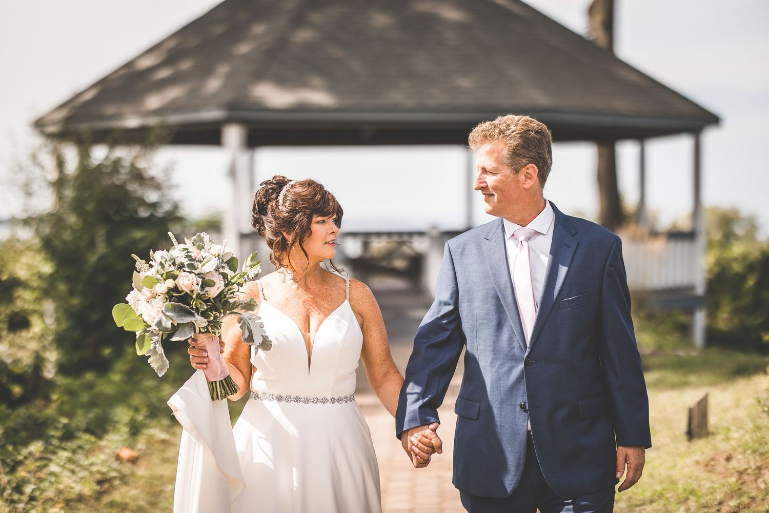 Newlyweds walk hand in hand along a scenic outdoor path during their wedding photoshoot.