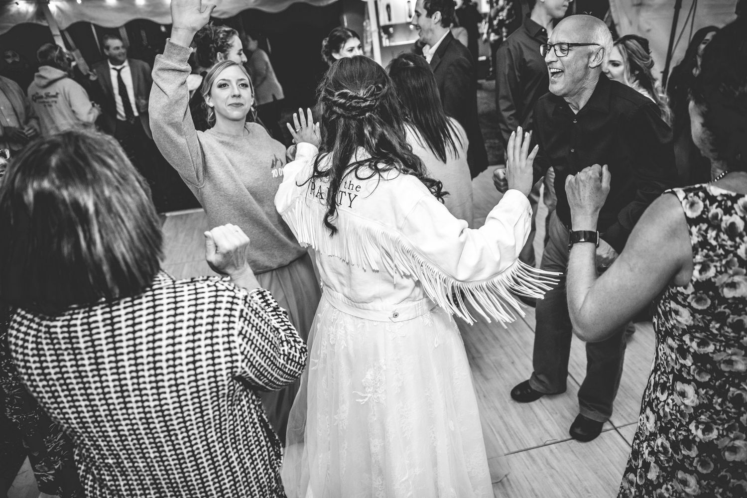 Black and white photo of guests dancing and celebrating at a wedding reception.